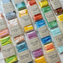 Load image into Gallery viewer, A variety of colored wax melt snap bars labeled with different fragrance names, arranged in rows on a surface.